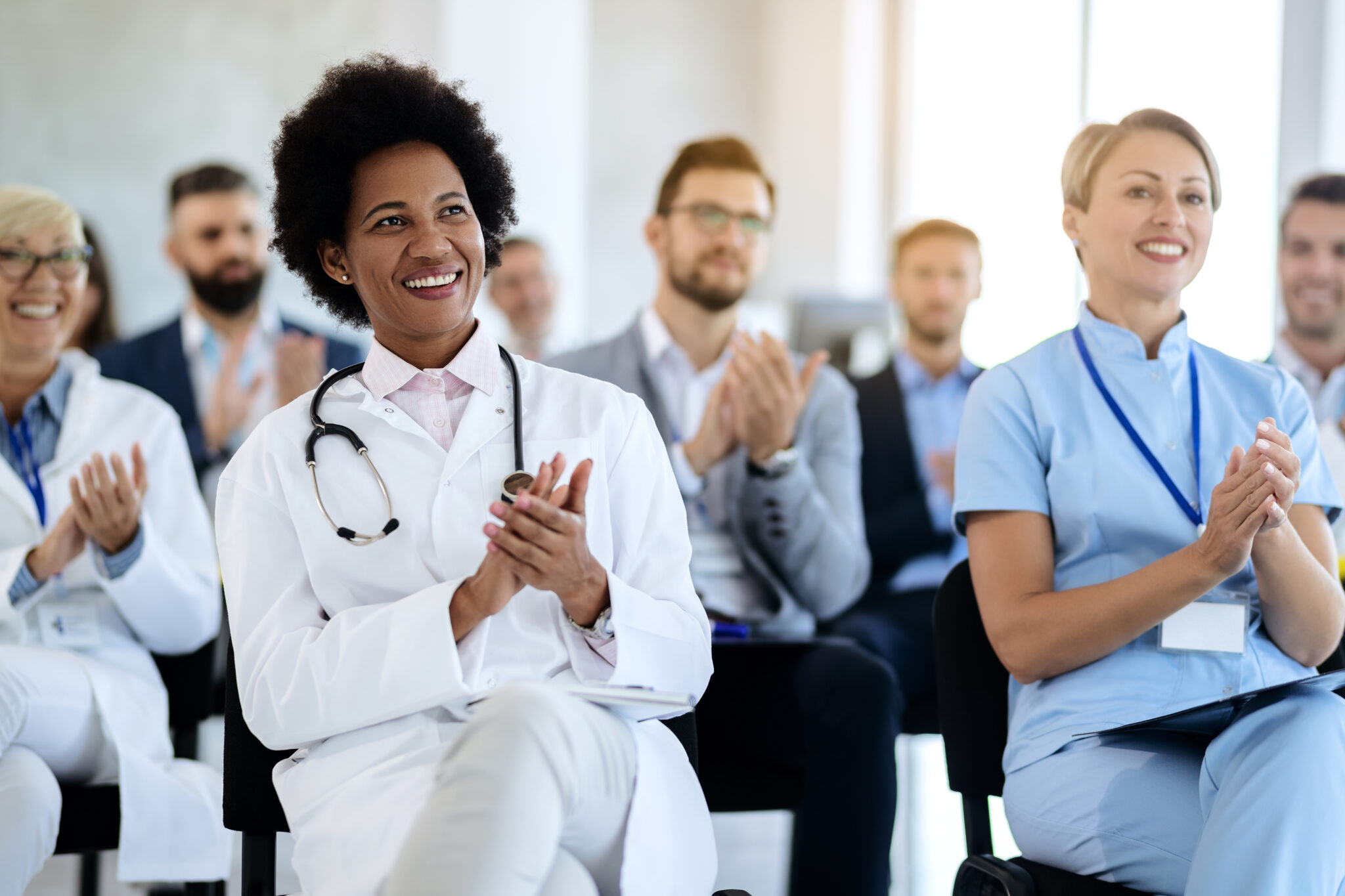 Happy black doctor and her colleagues clapping their hands after successful presentation in board room.